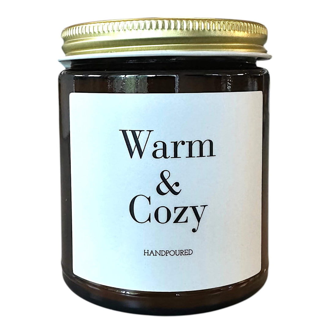 Amber glass candle with warm & cozy printed on front in black lettering