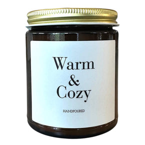Amber glass candle with warm & cozy printed on front in black lettering