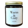 Amber glass candle with warm & cozy printed on front in black lettering