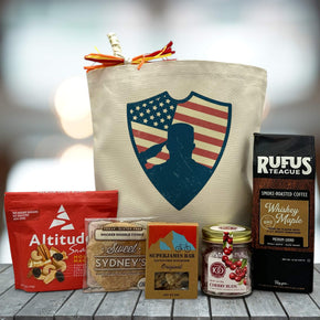 tote bag sitting on table with image of salute with trail mix, cookie, superjames bar, cherry buds, and coffee